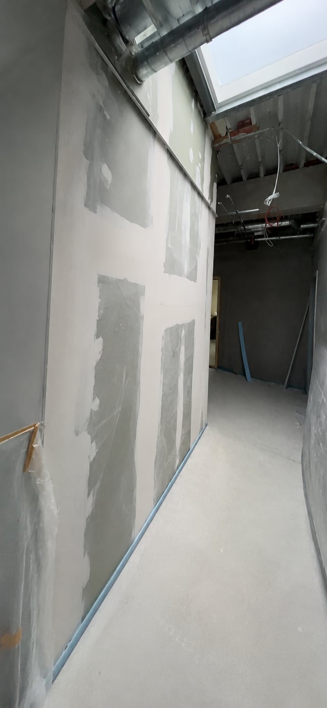 Flurbereich in Ingolstadt mit hoher, gespachtelter Trockenbauwand, Lüftungsleitung und Tageslicht durch ein Oberlicht